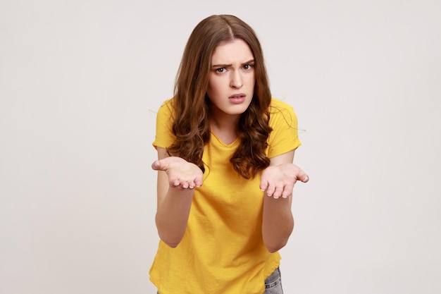 Comment pourriez-vous Portrait d'une adolescente malheureuse déçue en T-shirt jaune debout avec les mains levées demandant ce que vous voulez face en colère Studio tourné en intérieur isolé sur fond gris