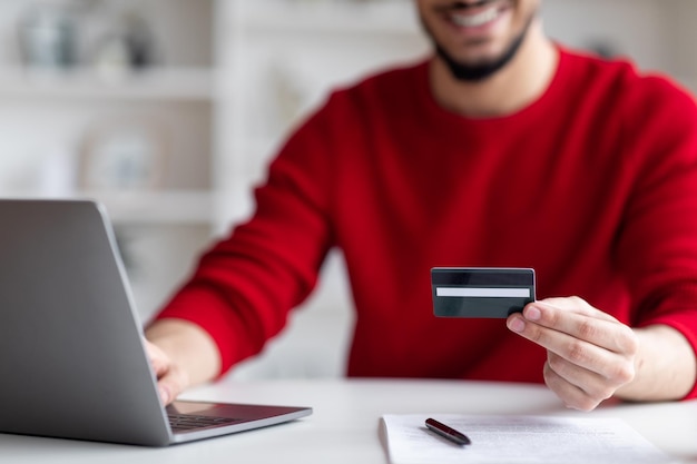 Commerce électronique souriant homme arabe utilisant un ordinateur portable et une carte de crédit pour les paiements en ligne