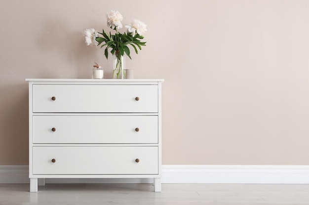 Commode blanche avec bouquet et bougie près du mur beige Espace pour le texte