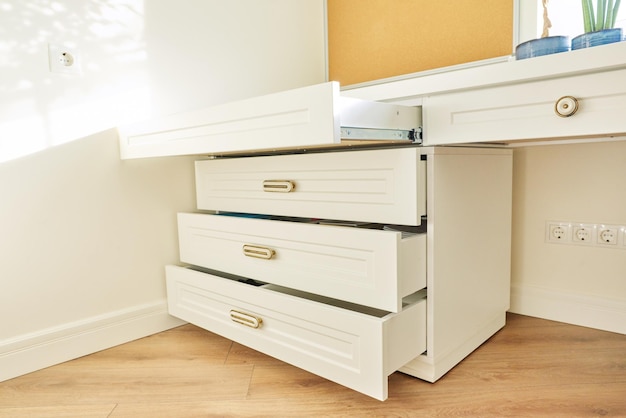 Photo commode en bois blanc avec poignées en bronze vintage sous le bureau à l'intérieur de la chambre des enfants, bureau à domicile