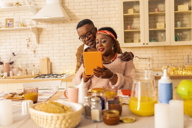 Communication agréable. Belle femme afro-américaine parlant à son mari tout en lui montrant l'écran de la tablette