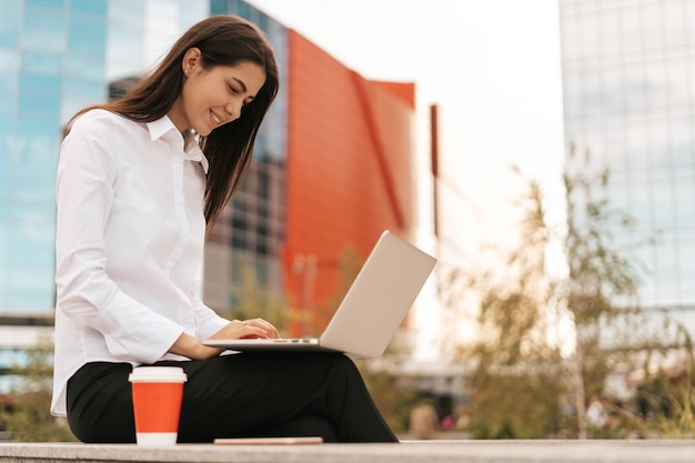 Communication d'entreprise. Femme d'affaires caucasienne parlant au téléphone portable travaillant sur ordinateur portable dans un bureau moderne.