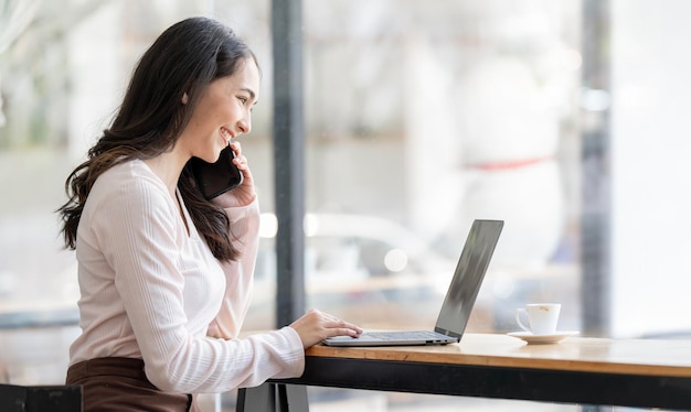 Communication d'entreprise Jeune femme d'affaires parlant sur téléphone portable et travaillant sur ordinateur portable dans un espace de travail