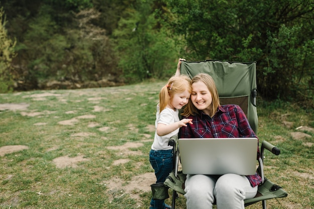 Communication avec la famille en ligne sur un ordinateur portable près du feu dans la nature