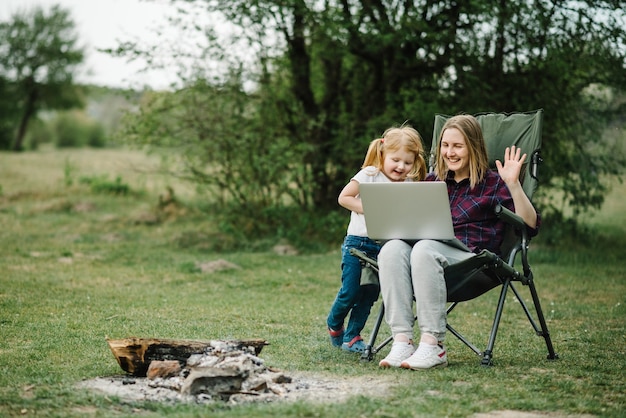 Communication avec la famille en ligne sur un ordinateur portable près d'un feu dans la nature