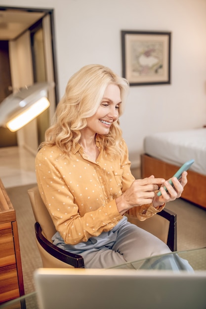 La communication. Jolie femme blonde assise dans un fauteuil avec un téléphone dans les mains