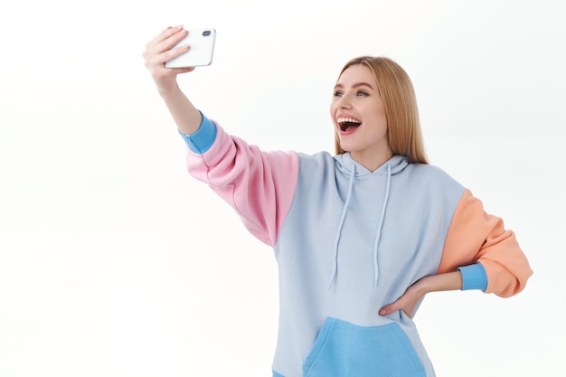 Communication, technologie et concept en ligne. Blogueuse blonde joyeuse, jeune fille prenant selfie sur smartphone