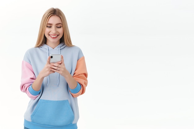 Communication, technologie et concept en ligne. Jolie fille européenne en sms à capuche, à l'aide de smartphone