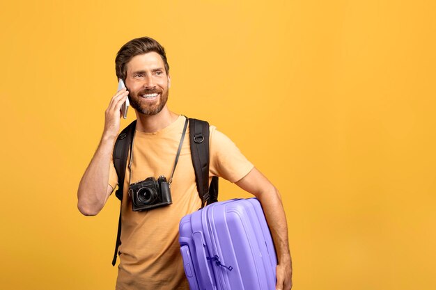 Communication de voyage homme d'âge moyen souriant parlant au téléphone portable tenant une valise et regardant de côté