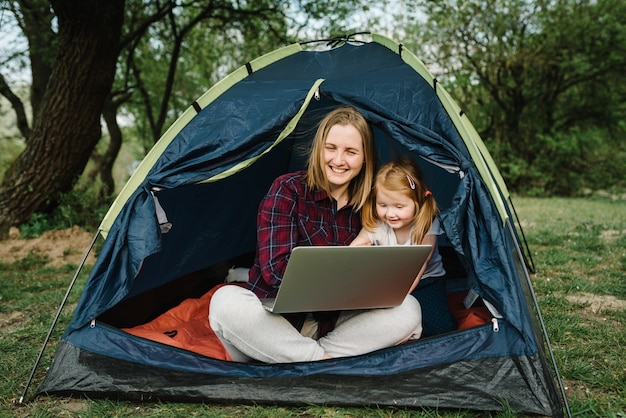 Communiquez avec vos proches, votre famille en ligne sur un ordinateur portable sous une tente dans la nature. Travailleuse parlent par appel vidéo avec des collègues. Mère travaillant avec enfant. L'enfant fait du bruit et dérange maman.