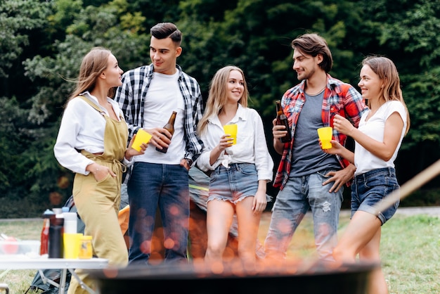 Une compagnie d’amis au camp soulève une bouteille de bière et s’amuse au camping