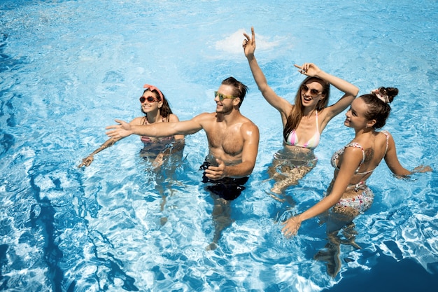 Compagnie de jeunes filles joyeuses et gars s'amusent dans la piscine en plein air par une journée d'été ensoleillée