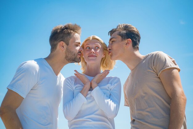 Une compagnie de jeunes gens heureux passe des loisirs à l'extérieur sur fond de ciel Des frères embrassent leur sœur surprise Deux garçons et une femme blonde sur fond de ciel d'été bleu