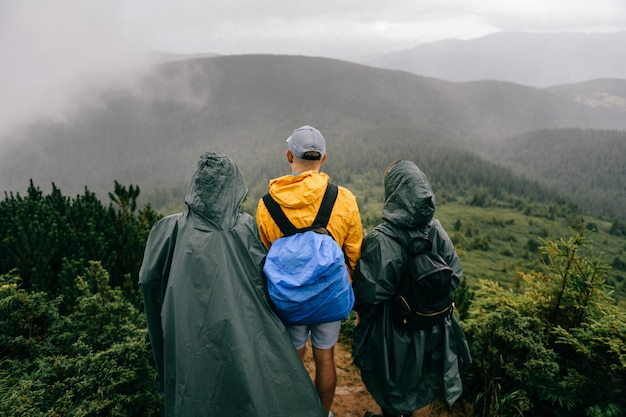 Une compagnie de voyageurs en imperméables se dresse au sommet de la montagne. Amis, apprécier, nature, vue, pluvieux, jour brumeux