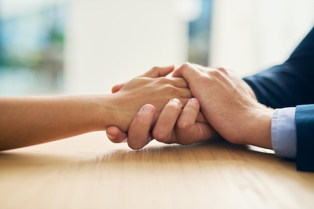 Compassion parfois un nom parfois un verbe Photo recadrée d'un homme d'affaires et d'une femme d'affaires se tenant la main avec compassion à une table