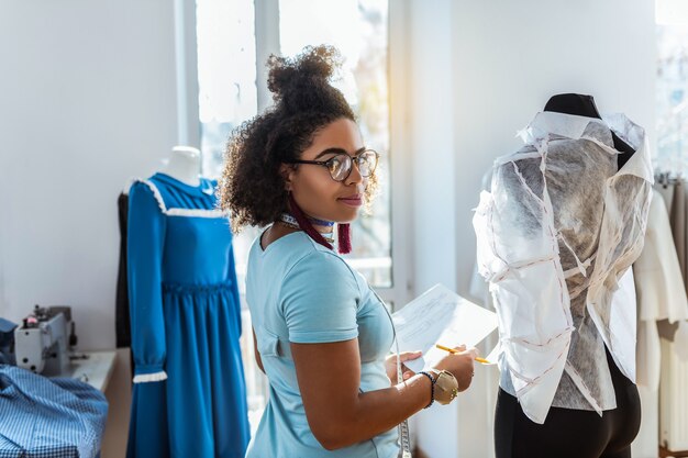 Photo compléter la nouvelle tenue. femme afro-américaine souriante à l'aide de mannequin pour la construction et la connexion de pièces de costume