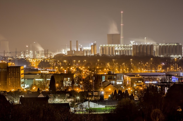 Complexe industriel la nuit, structures métalliques et cheminées avec reflet de lampes jaunes