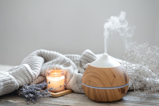 Composition d'arôme avec un diffuseur d'huile d'arôme moderne sur une surface en bois avec un élément tricoté, une bougie et de la lavande.