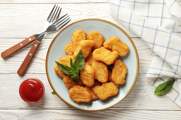 Composition avec assiette de pépites de poulet sur fond de bois blanc