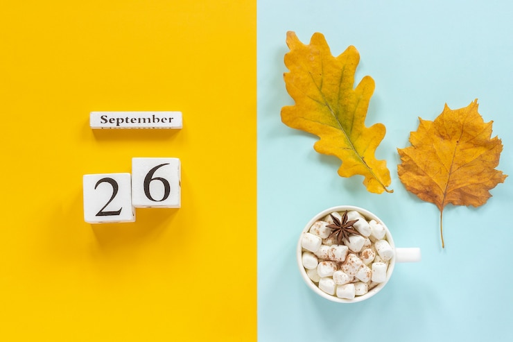 Photo composition d'automne. calendrier en bois 26 septembre, tasse de cacao avec guimauves et feuilles d'automne jaunes sur fond bleu jaune. vue de dessus concept de maquette à plat bonjour septembre.