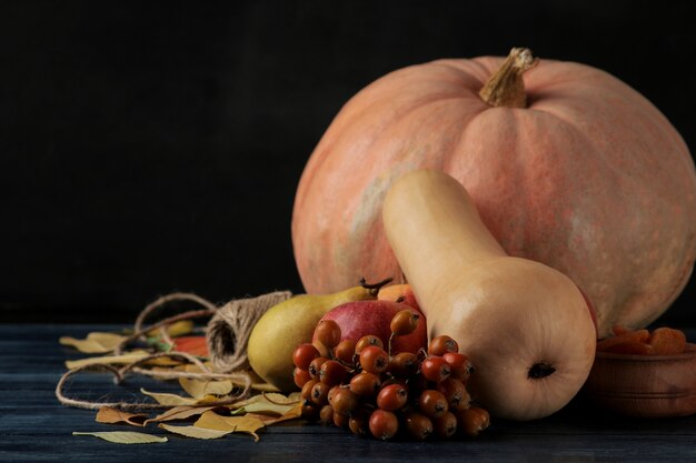 Composition d'automne avec citrouille et fruits d'automne avec pommes et poires sur une table bleu foncé et sur fond noir