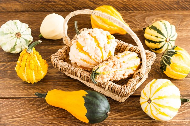 Composition d'automne de citrouilles de différentes formes dans un panier sur un fond en bois.