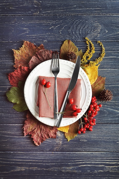 Photo composition d'automne de feuilles, baies, assiette, couteau et fourchette sur fond en bois. concept de jour de thanksgiving