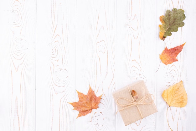 Composition d'automne avec des feuilles sèches d'automne un cadeau emballé dans du papier kraft disposé dans un coin sur un fond en bois blanc rustique Espace de copie plat