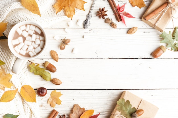 Composition d'automne Foulard foncé une tasse de cacao avec des guimauves feuilles sèches d'automne sur une table en bois blanc Vue de dessus Espace de copie