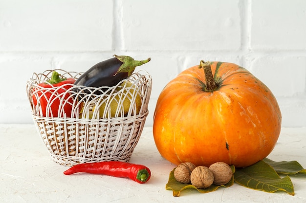 Composition d'automne avec une grosse citrouille et des légumes. Citrouille et panier en osier avec un poivron, une aubergine sur fond blanc. Achats d'automne. Jour de Thanksgiving.