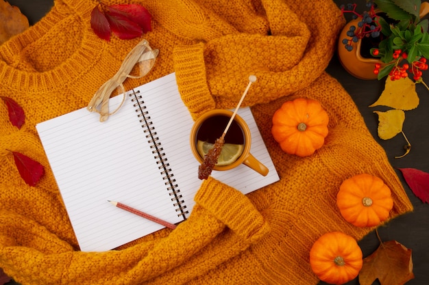 Composition d'automne à plat avec des feuilles d'automne, une tasse de thé chaude et un pull orange chaud en laine