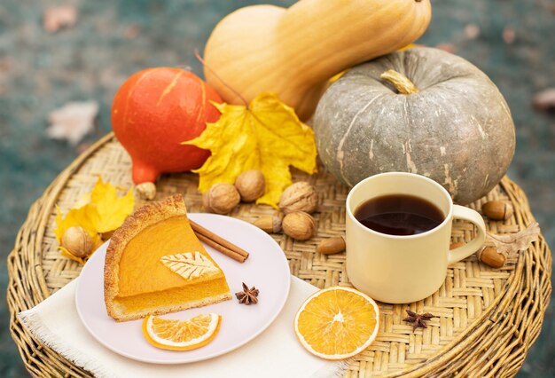 Composition d'automne de tarte à la citrouille avec une tasse de thé chaud sur une table en osier et des citrouilles dans le jardin