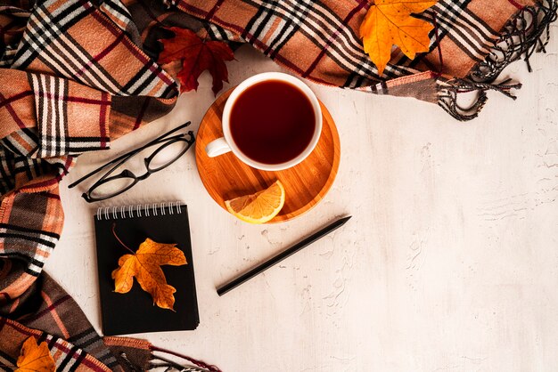 Composition d'automne. Une tasse de thé, une écharpe, des feuilles d'automne, des lunettes, un bloc-notes, un crayon. Mise à plat, vue de dessus, espace de copie. photo de haute qualité