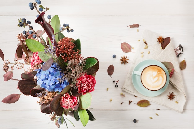 Composition de cappuccino d'automne. Vue de dessus de tasse à café bleu avec mousse, clous de girofle, bouquet de fleurs séchées à table en bois blanc. Concept de boissons chaudes, café et bar d'automne