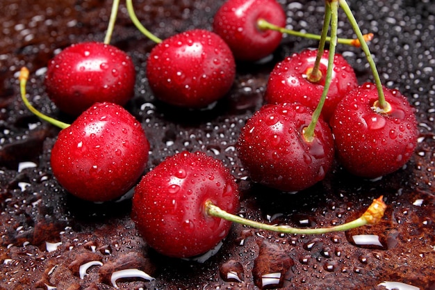 Composition de cerises douces sur fond sombre avec vue de dessus de gouttes d'eau. Gros plan de grosses cerises rouges