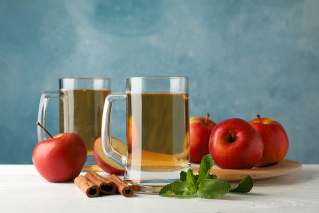 Composition avec cidre, cannelle et pommes sur table en bois blanc