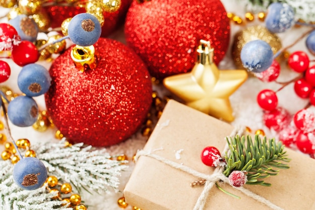 Composition colorée de Noël avec des boules rouges cadeaux baies de houx branche d'arbre de Noël et guirlande dorée sur fond de neige blanche