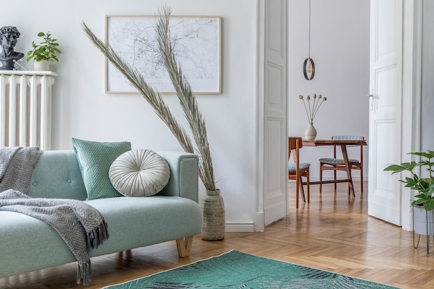 Composition confortable et créative d'un design d'intérieur de salon élégant avec cadre, canapé vert, meubles en bois, plantes et accessoires. Murs blancs, parquet au sol.
