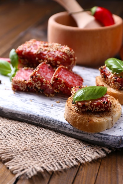 Composition avec couteau savoureux sandwiches avec feuille de basilic saucisse salami sur planche à découper sur fond de bois