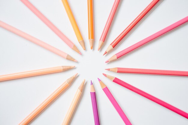 Composition de crayons de couleur chaude rythmés en motif solaire sur blanc