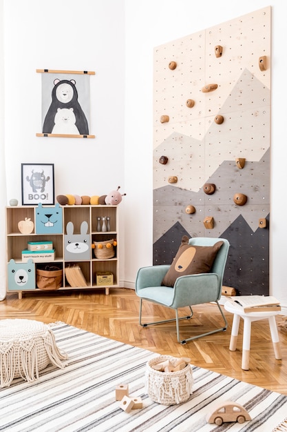 Composition créative d'un design d'intérieur de chambre d'enfant scandi élégant et confortable avec des graphiques sur le mur jouets et jouets en peluche canapé commode fauteuil tapis et accessoires Mur blanc et parquet