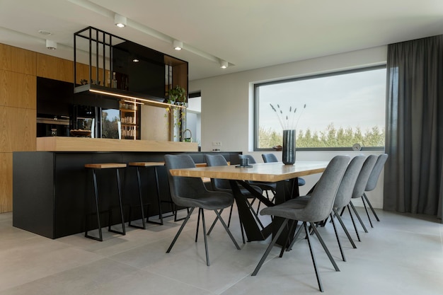 Composition créative du design d'intérieur de la salle à manger et de la cuisine à aire ouverte. Table familiale rectangulaire, chaises en velours, cuisine intégrée ergonomique en bois et accessoires personnels élégants. Modèle.