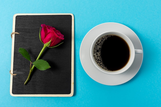 Composition créative de fleur rose rouge et tasse de café sur bleu.