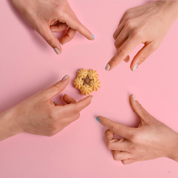 Photo composition créative des mains atteignant le cookie sur fond rose