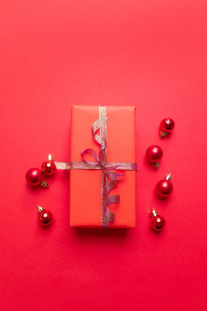 Composition créative de Noël avec une boîte à cadeaux rouge, des rubans, des boules petites et grandes rouges, des décorations de fêtes rouges. Pose à plat, vue de dessus, surface