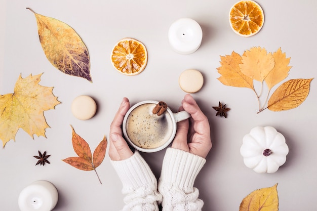 Composition créative plate d'automne. Les mains des femmes tiennent une tasse de café à la cannelle.