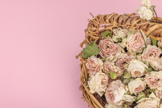 Composition créative avec des roses sèches et délicates dans un panier en osier fait maison Carte de vœux à fond rose pastel