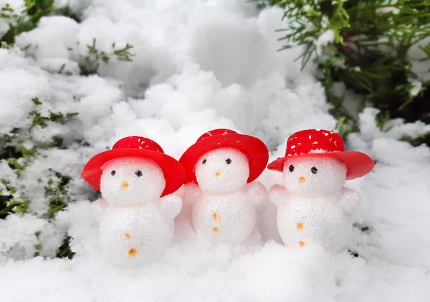 Composition décorative de Noël et de bonne année de drôles de trois bonhommes de neige en chapeaux rouges debout dans la neige. Paysage de Noël de célébration. Vue latérale, arrière-plan avec espace de copie pour votre texte