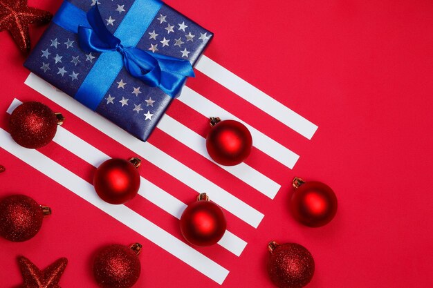 Composition du drapeau américain avec un cadeau bleu décoré d'étoiles scintillantes et de décorations d'arbres de Noël sur fond rouge. Joyeux noël et bonne année concept.