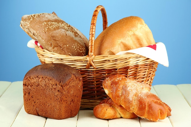 Composition avec du pain et des petits pains dans un panier en osier sur une table en bois sur fond de couleur